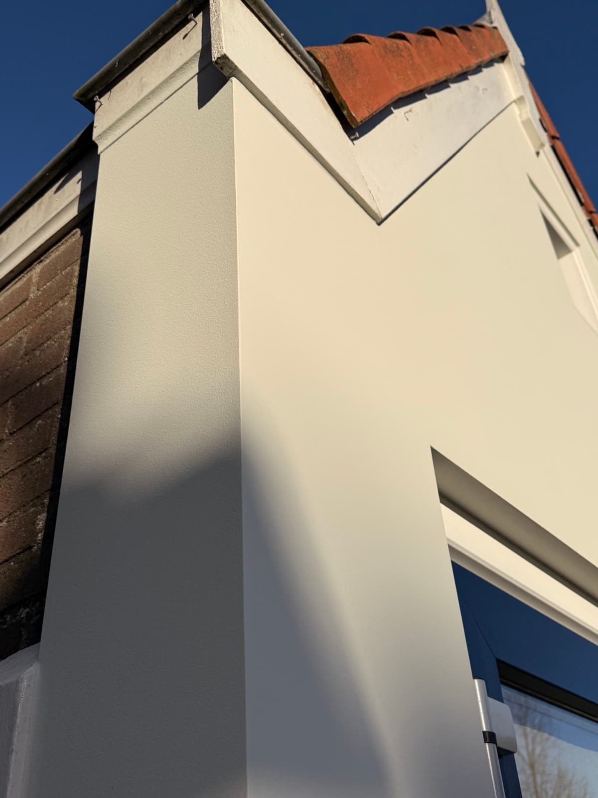 Detail glad gevelstucwerk bij dakrand met strijklicht